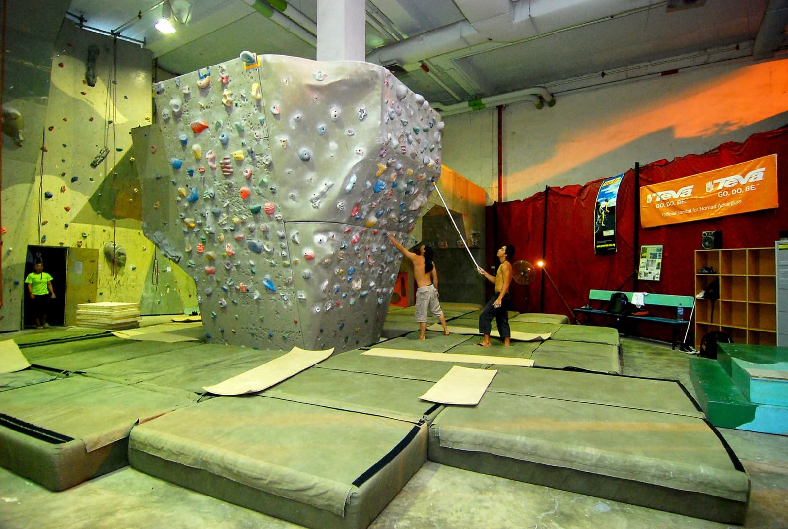 An indoor climbing gym with a colourful bouldering wall above thick crash mats.