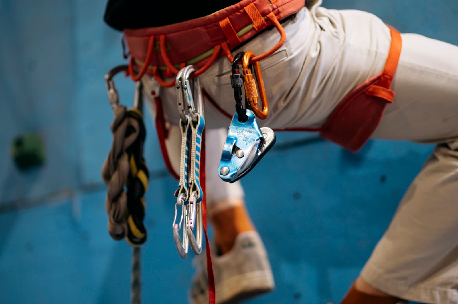 A climber at an indoor gym with a harness and safety gear, ready to start a route.
