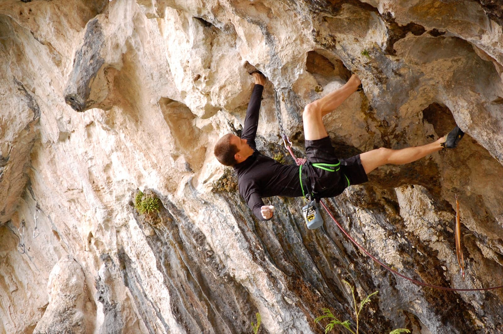 A climber on a steep outdoor rock face on a sunny day.