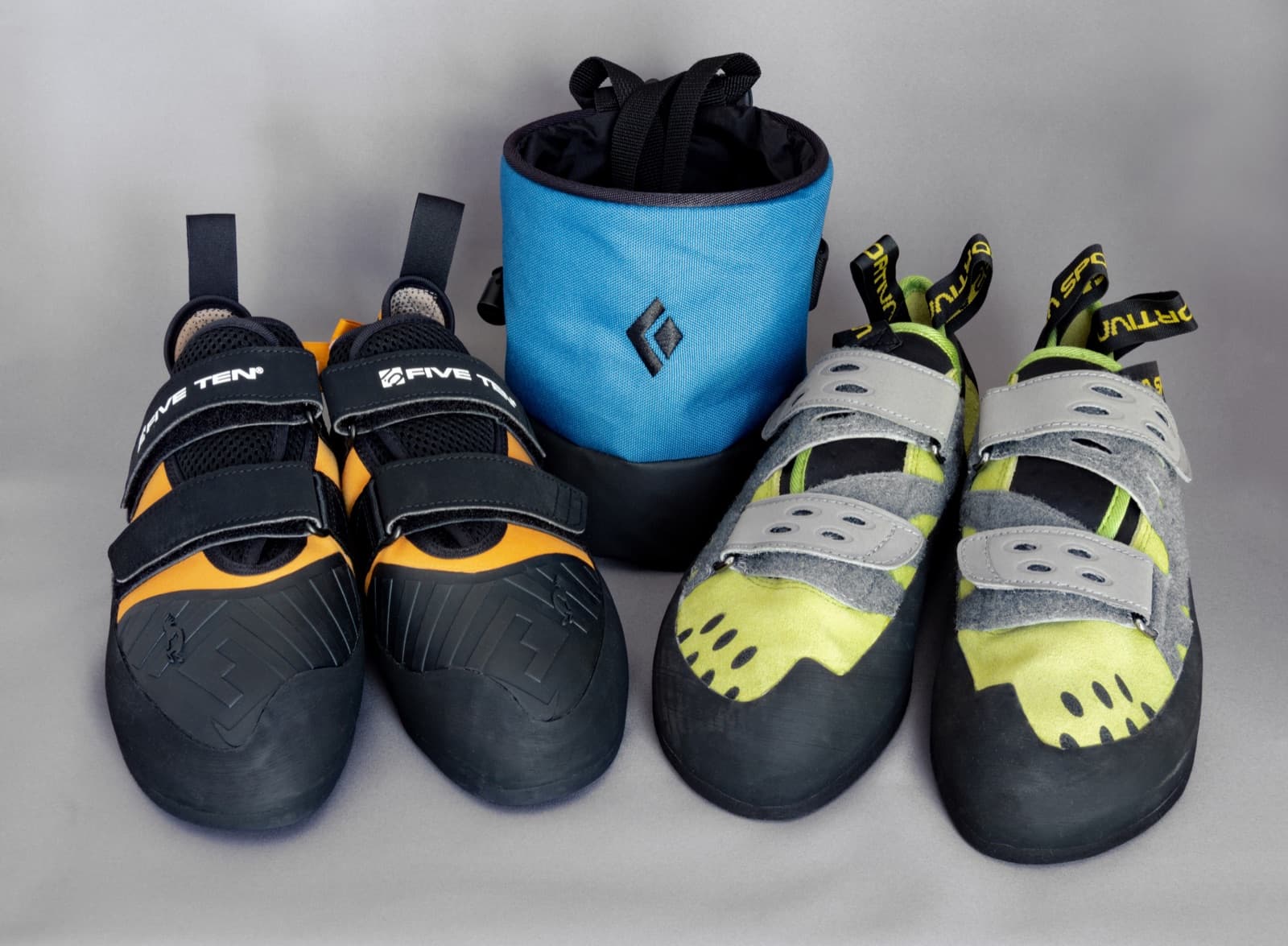A pair of climbing shoes next to a chalk bag on a wooden surface.