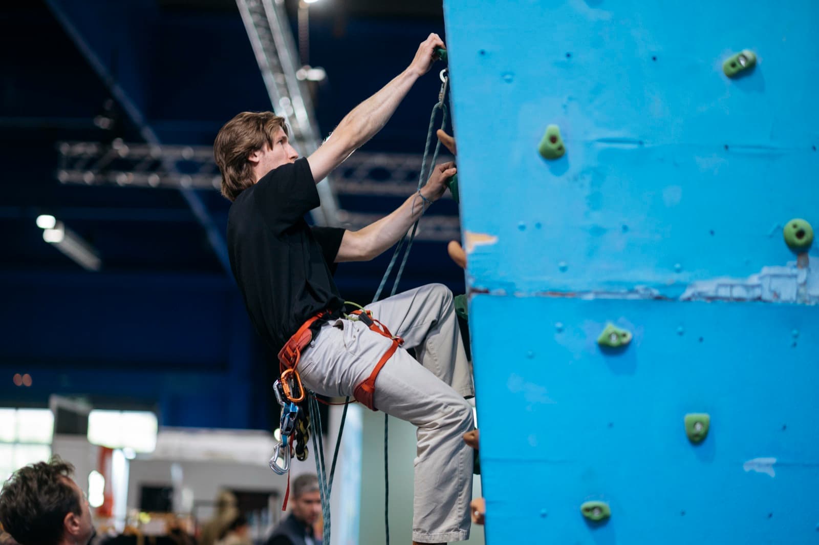 Climbers on an indoor climbing wall at a busy gym.