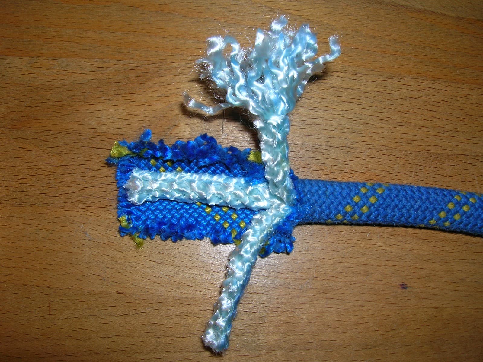 A close-up of a damaged climbing rope with a frayed sheath exposing the inner fibres.