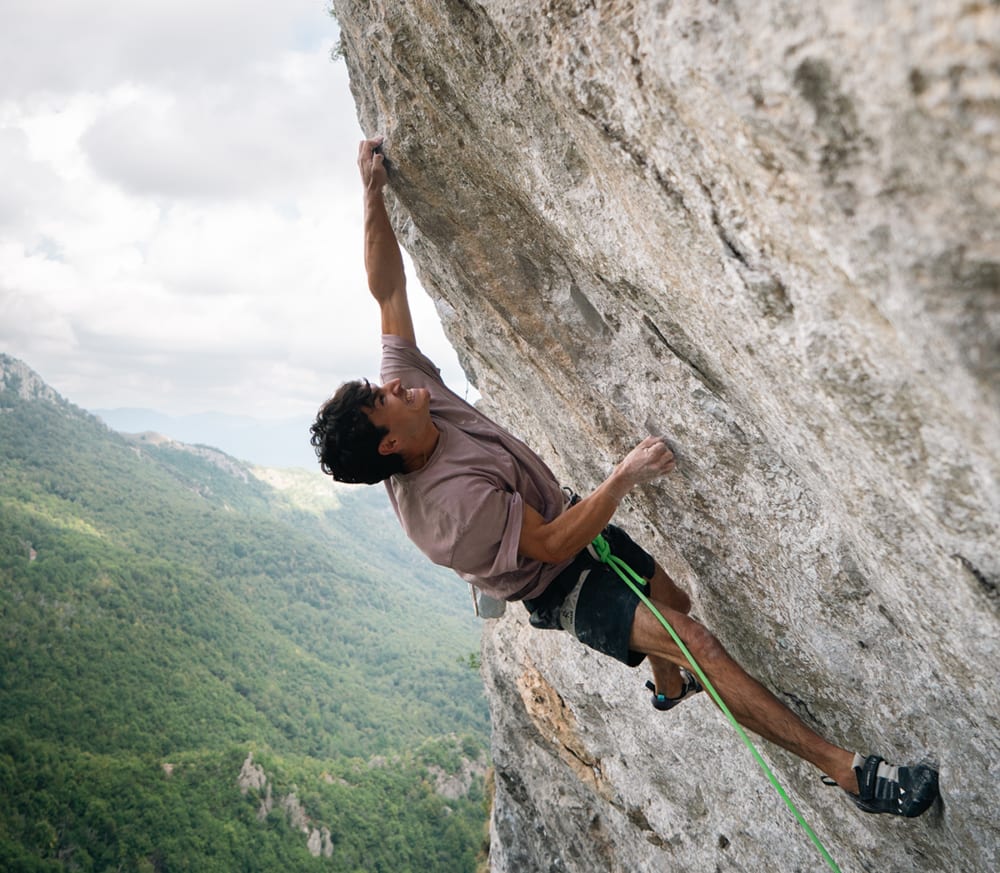 Giovanni Placci climbing a steep grey limestone wall above a wooded valley