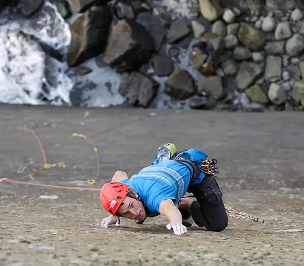 Climber in a red helmet crawling across a rocky ledge