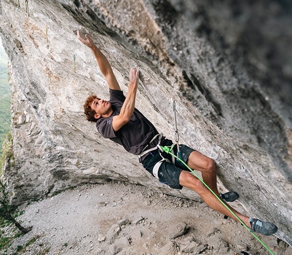 Climber in a black T-shirt leaning out on a steep grey limestone overhang with the rope clipped below
