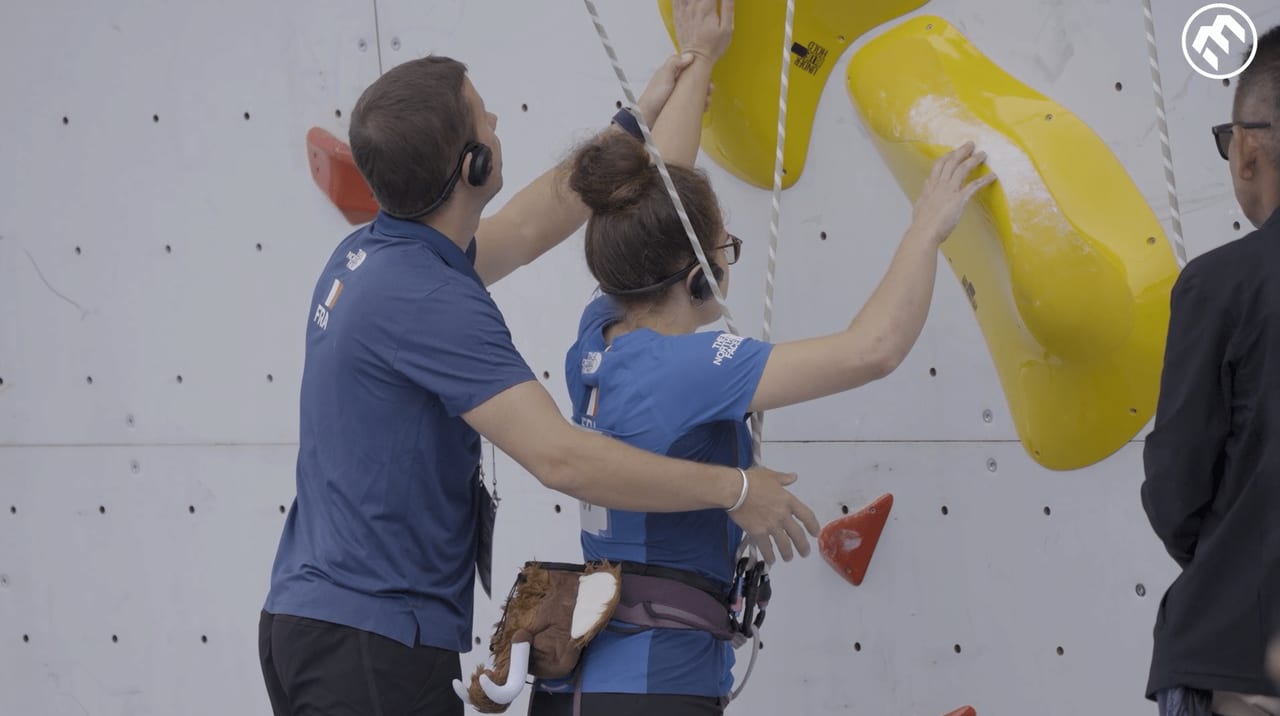Instructor guiding a climber's hand towards a hold on an indoor wall
