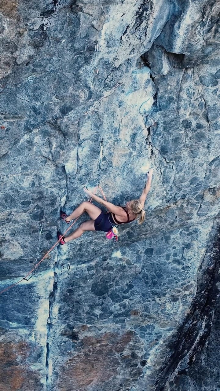 Climber in a pink top on a blue grey pocketed limestone face