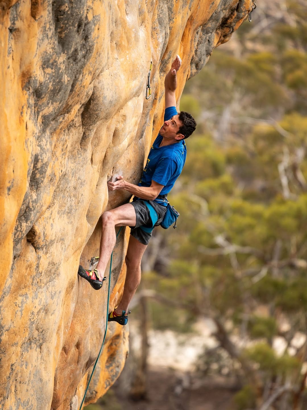 Climber in a blue shirt on a steep orange sandstone face at Mount Arapiles