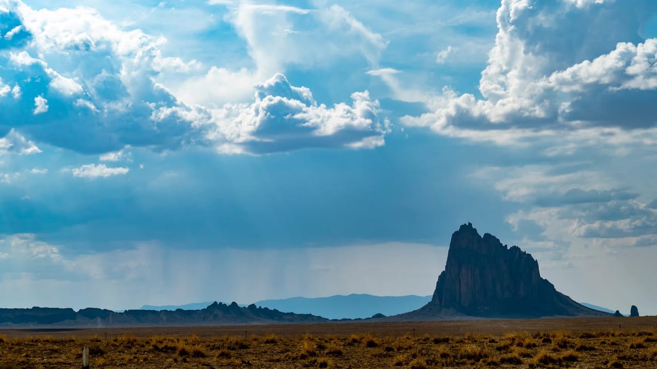 A lone desert rock spire under rain clouds