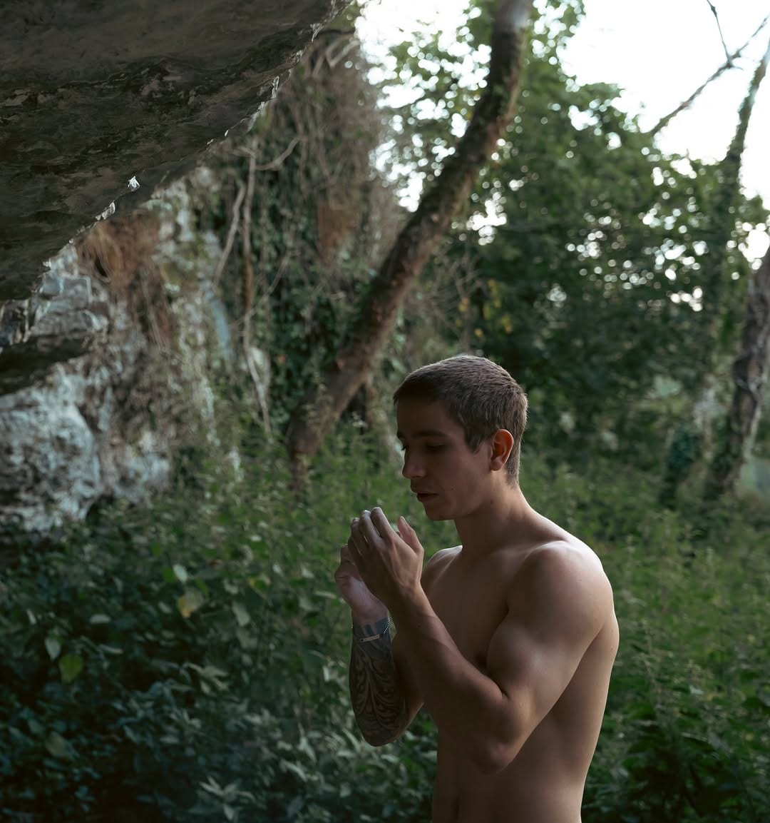 Matthew Mendess chalking his hands under a limestone overhang in the woods