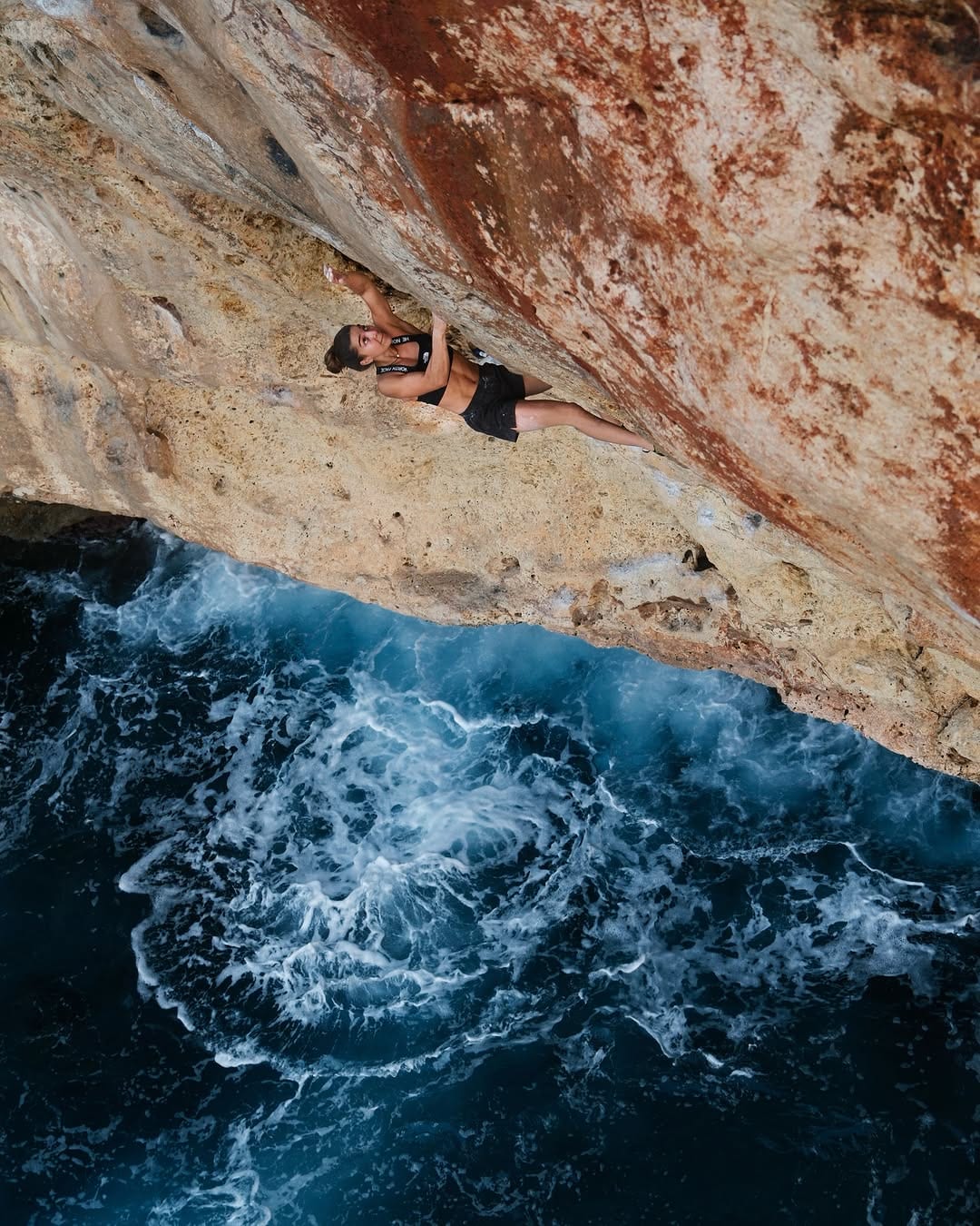 Brooke Raboutou climbing a sea cliff overhang above breaking waves