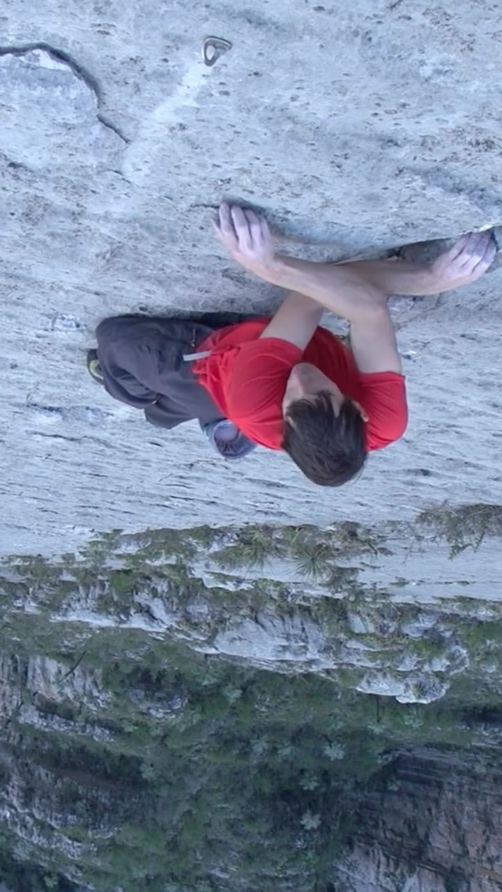 Alex Honnold climbing grey limestone without a rope, high above a green valley
