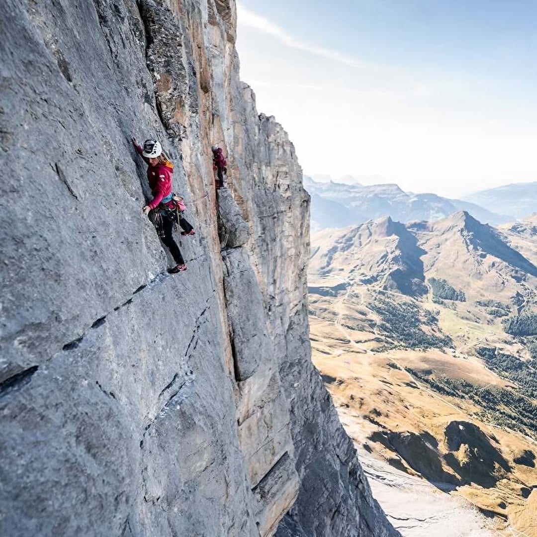 Fay Manners on a steep grey wall of the Eiger North Face, with her partner above and the valley far below