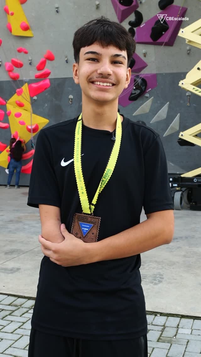 João smiling with his medal in front of a climbing wall