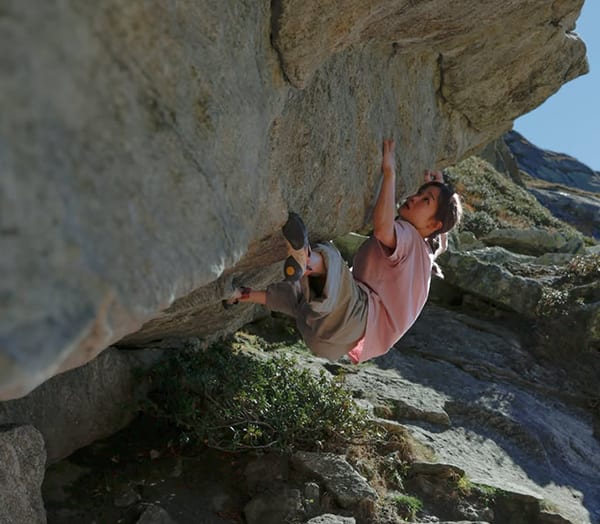 Mei Kotake in a pink shirt climbing the underside of a granite roof at the Gotthard Pass