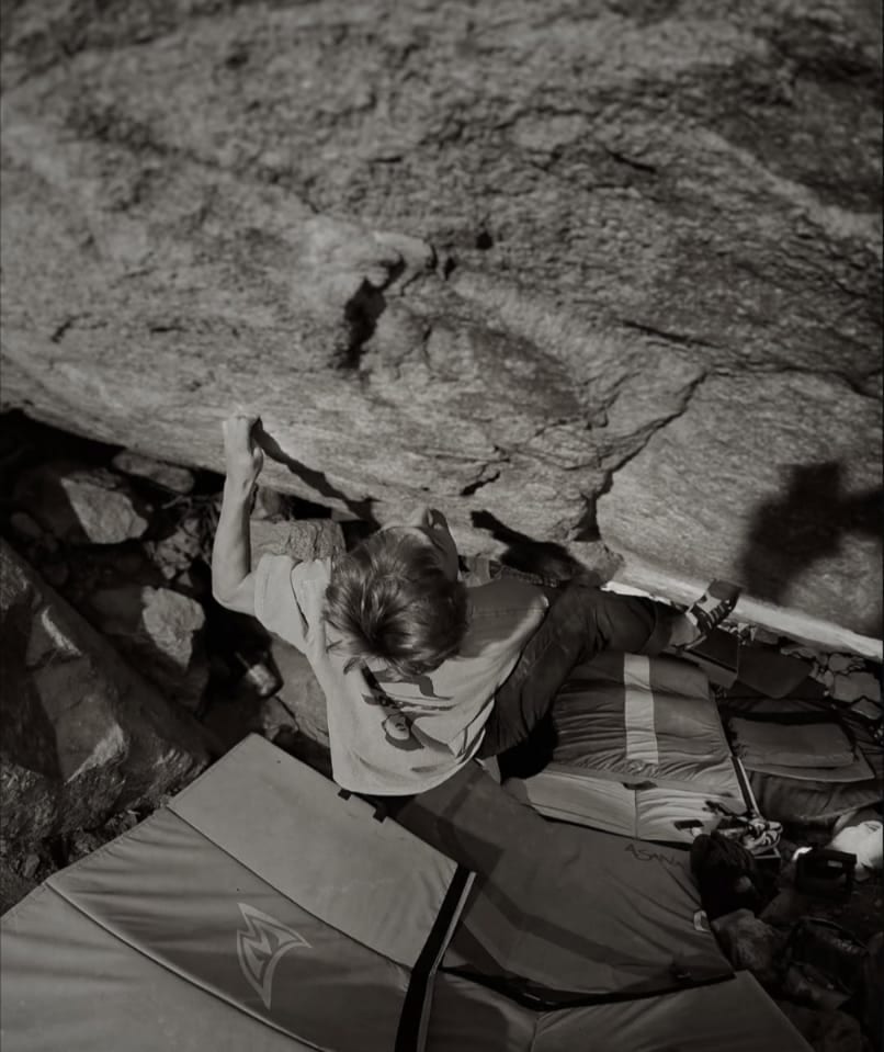 Black and white photo of a climber under a granite roof above crash pads